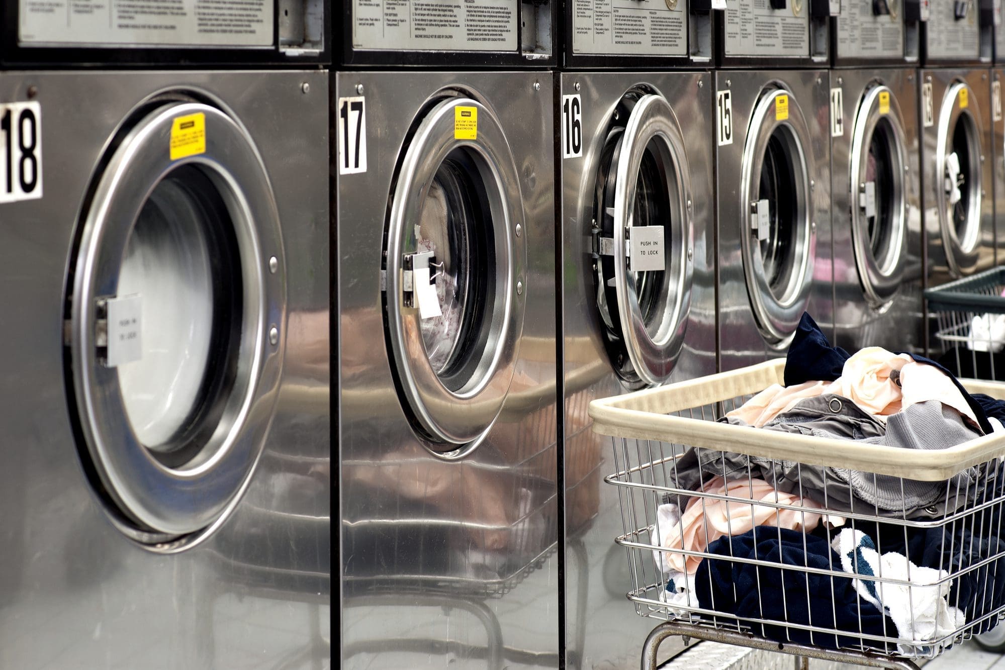 Row of washing machines in a laundromat with laundry carts in the foreground.