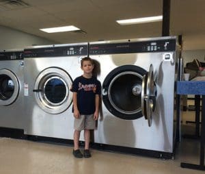 A child standing in front of industrial washing machines at a laundromat.