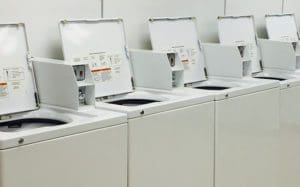 A row of open-top washing machines in a laundromat awaits the answer to "How Much Detergent Should I Be Using?