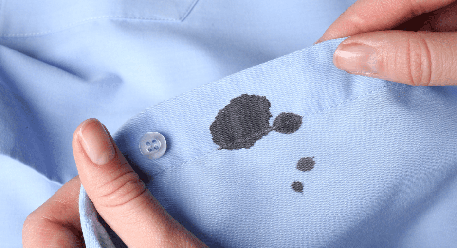 A close-up of hands holding a blue shirt with an ink stain near the buttoned cuff use Hydrogen Peroxide in Laundry