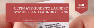 Close-up of hands holding a fabric care label. Overlaid text reads, "Ultimate Guide to Laundry Symbols and Laundry Signs." The Dutchman’s Laundry logo is in the upper right corner.