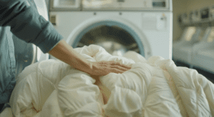 A person places their hand on a white comforter in front of a washing machine. How to Wash Your Comforter At The Laundromat.