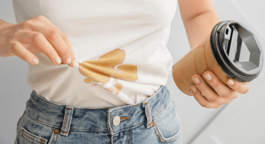 Person holding a coffee cup spills coffee on their white t-shirt, wearing blue jeans. hot or cold water for stains.