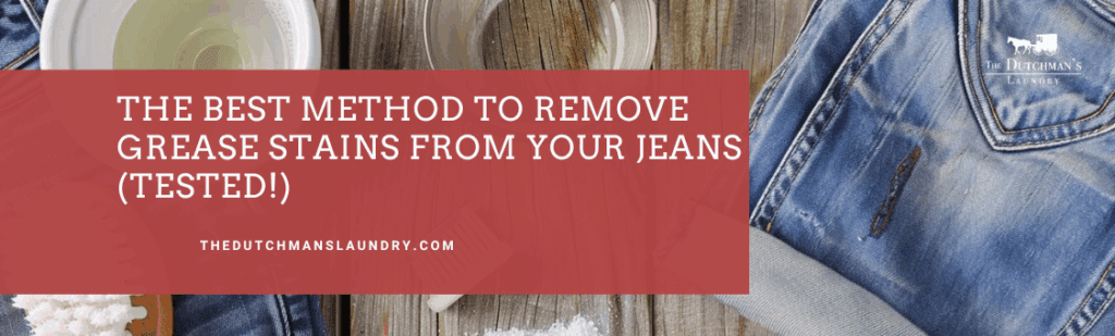 A pair of blue jeans with a grease stain sits on a wooden surface next to a bowl of liquid, a white towel, and a small container of powder.