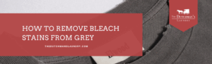 Close-up of a grey shirt with a visible bleach stain and a label, overlaid with text: “How to remove bleach stains from grey” and The Dutchman’s Laundry logo.