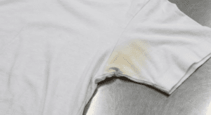 A white t-shirt lying on a metallic surface with a visible yellowish stain in the armpit area.