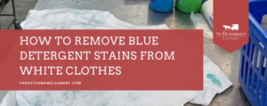 A white shirt with blue detergent stains lies on a table next to cleaning bottles and a blue laundry basket. Text reads, "How to remove blue detergent stains from white clothes.