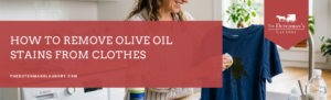 Woman treating an olive oil stain on a blue shirt in a laundry room; text overlay reads “How to remove olive oil stains from clothes.”.